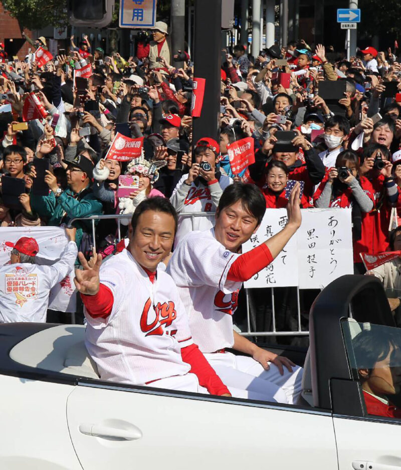 2016年シーズンのリーグ優勝を果たし引退したオフシーズンに広島市内で行われた優勝記念パレードにて、沿道のファンに手をふる広島カープの黒田博樹と新井貴浩