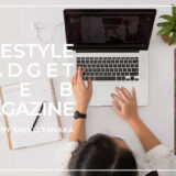 手帳と雑誌をデスクに広げながらMacBookでWEBマガジン・ブログの記事執筆の仕事をする女性の様子