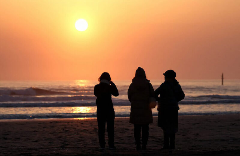 2022年3月11日午前6時過ぎ、福島県いわき市の薄磯海岸で朝日を見つめる人たち